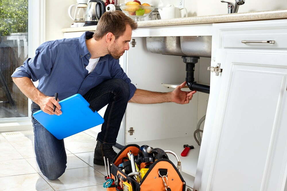A plumber inspects pipes under a sink